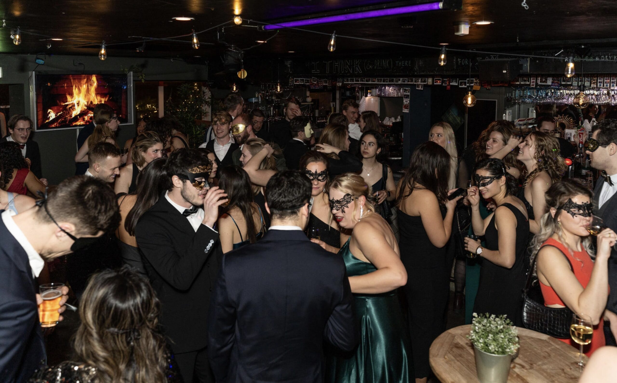 Gemaskerd bruiloftsfeest met dansende gasten in een sfeervol verlichte zaal